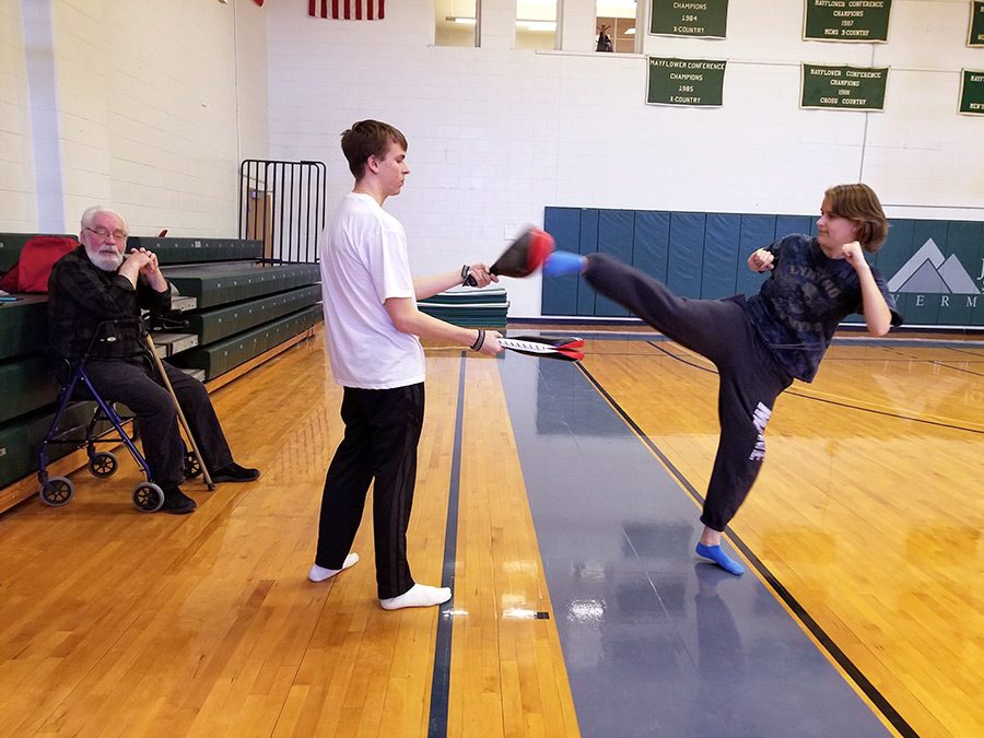 (Left to right) Stanley Parsons watches while John Whitney holds paddles and Amber Downs throws a round-house kick