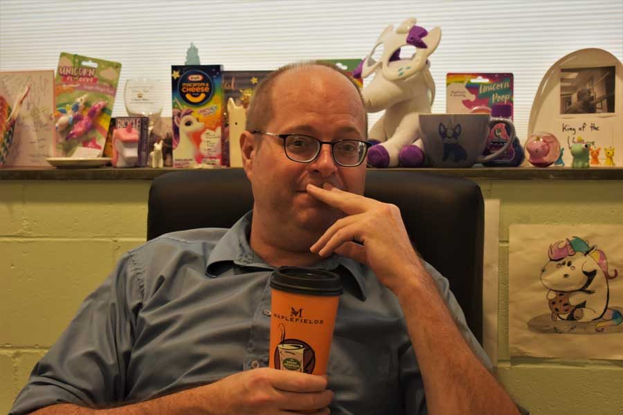 Shane Stacey sits in his office, coffee cup in hand and unicorn shrine behind him